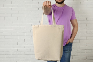 Photo of Man with cotton shopping eco bag against brick wall. Mockup for design
