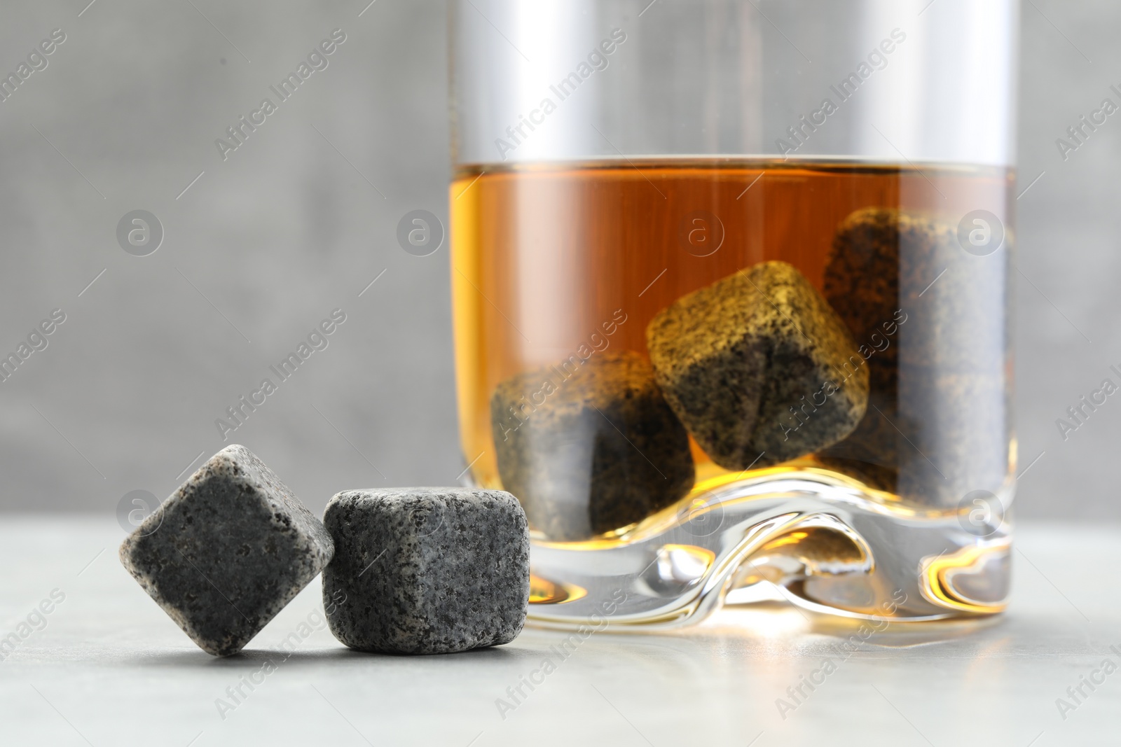 Photo of Whiskey stones and drink in glass on light table, closeup