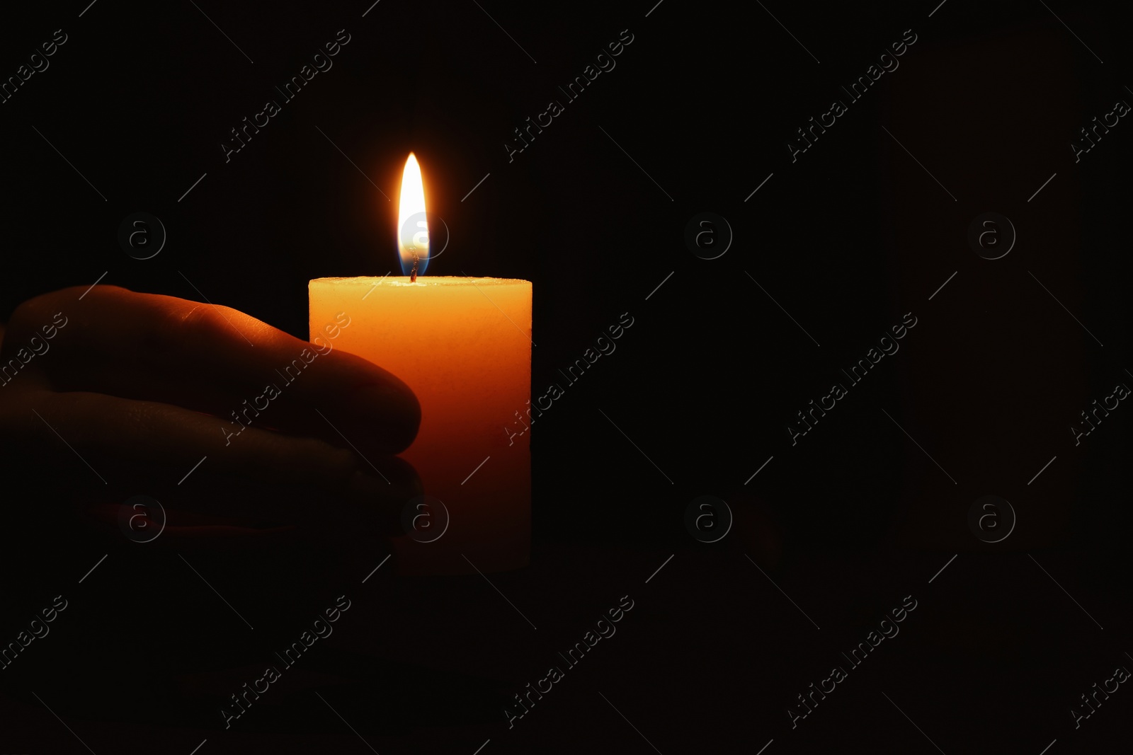 Photo of Woman holding burning candle in hand on black background, closeup. Space for text