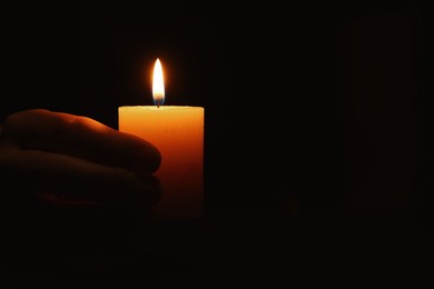 Photo of Woman holding burning candle in hand on black background, closeup. Space for text