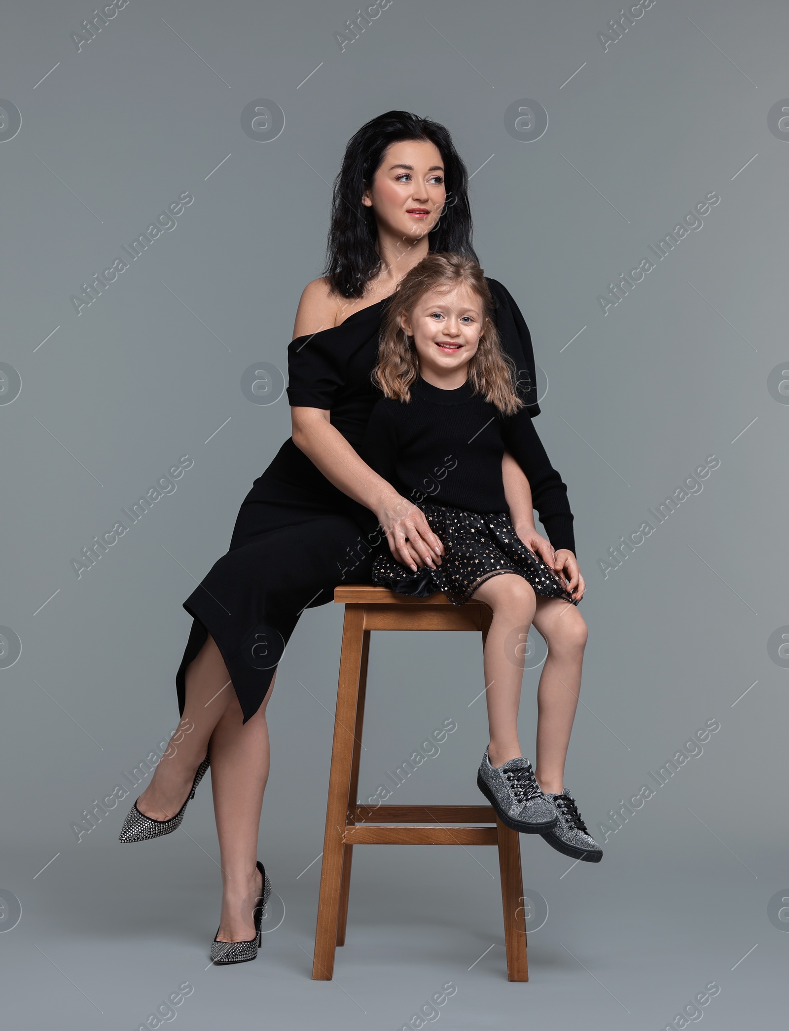 Photo of Beautiful mother with little daughter on stool against grey background