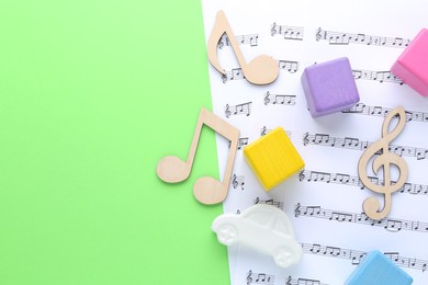 Wooden notes, music sheets and toys on light green background, top view with space for text. Baby song concept