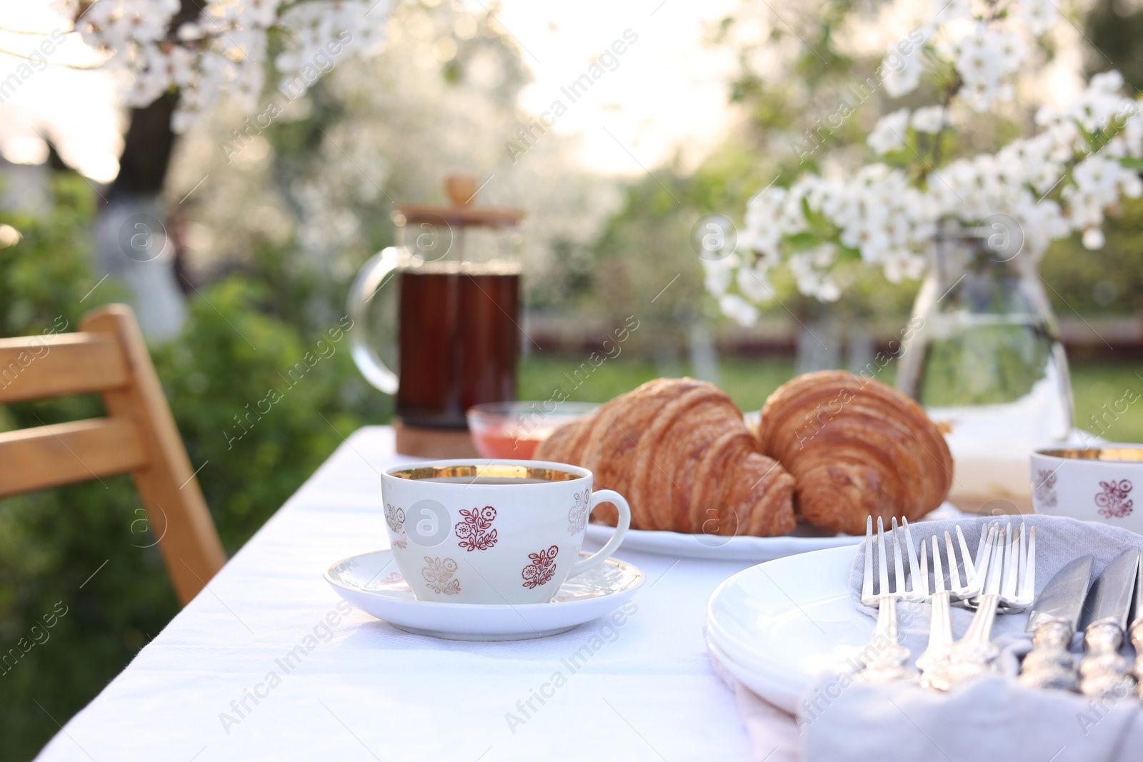 Photo of Stylish table setting with tea and croissants in spring garden