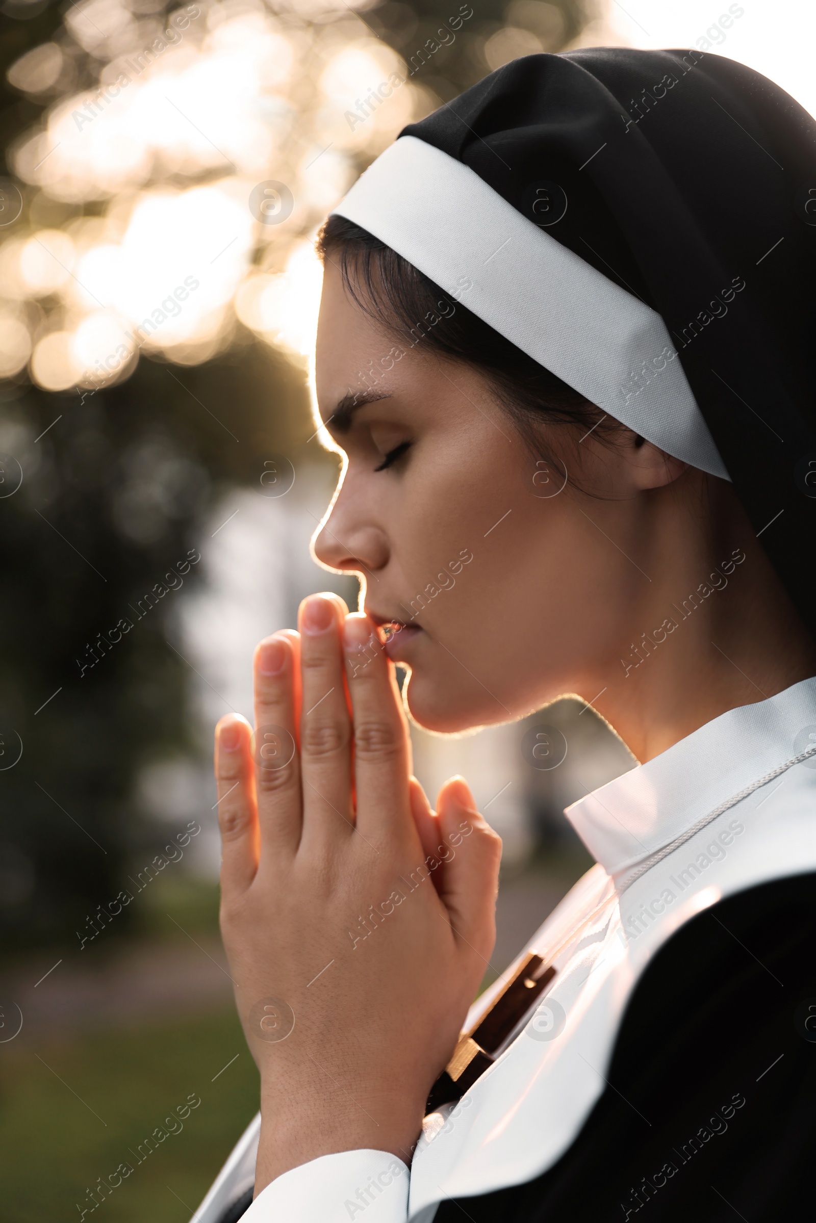 Photo of Young nun with hands clasped together praying outdoors on sunny day