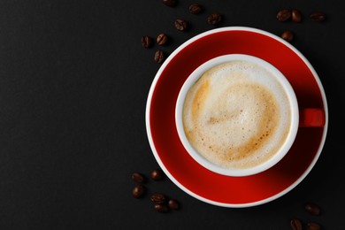 Photo of Cup with aromatic cappuccino and beans on black background, flat lay. Space for text