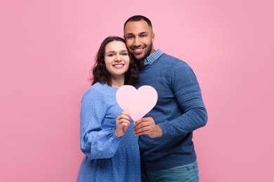 Lovely couple with paper heart on pink background. Valentine's day celebration