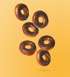 Image of Many fresh bagels with poppy seeds falling on light orange background