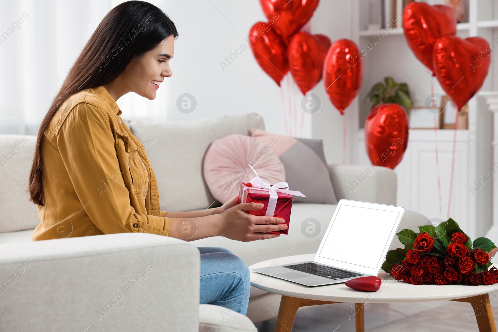 Photo of Valentine's day celebration in long distance relationship. Woman holding gift box while having video chat with her boyfriend via laptop at home