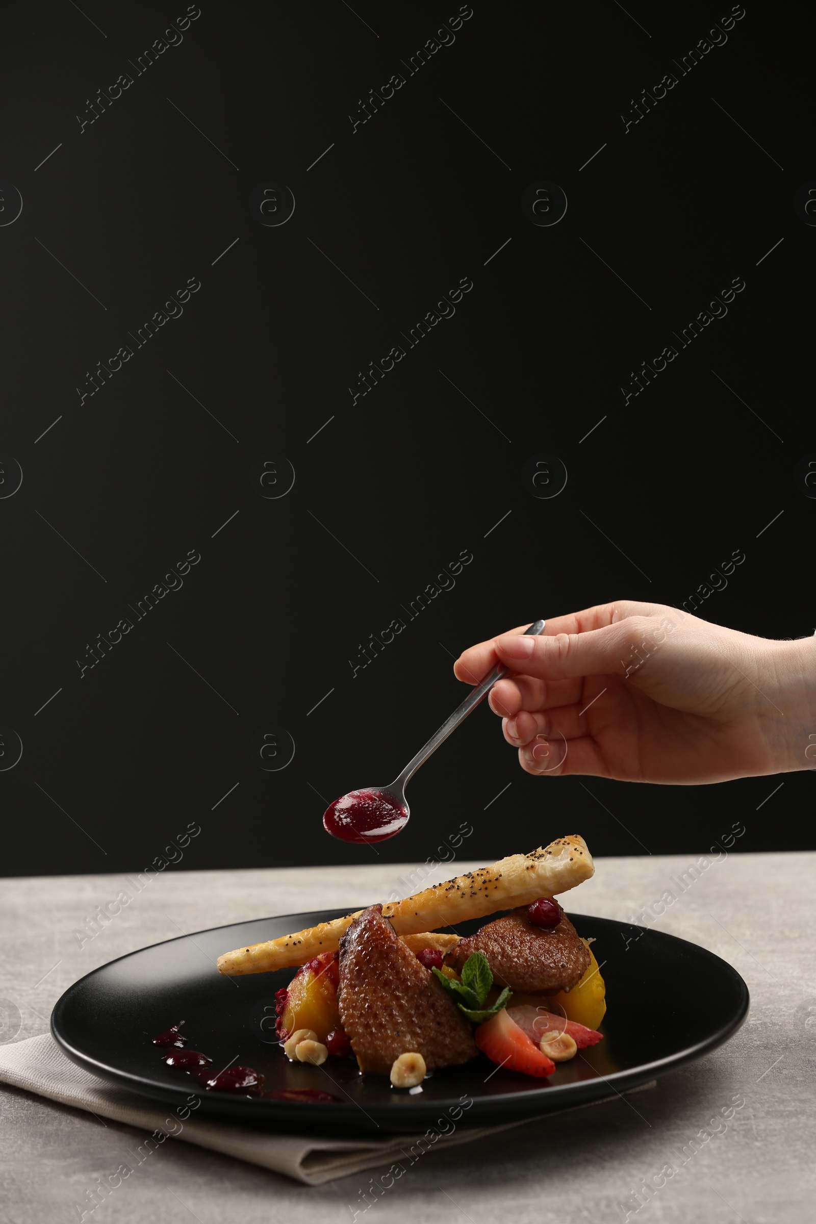 Photo of Food stylist adding sauce to delicious dish with chicken, parsnip and strawberries for photoshoot at grey table in studio, closeup