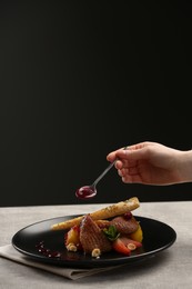 Photo of Food stylist adding sauce to delicious dish with chicken, parsnip and strawberries for photoshoot at grey table in studio, closeup