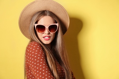 Photo of Young woman wearing stylish sunglasses and hat on yellow background