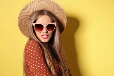 Young woman wearing stylish sunglasses and hat on yellow background