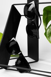 Photo of Stylish sunglasses hanging on black shelf against white background