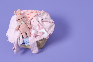 Laundry basket with baby clothes and soft toy on light purple background. Space for text