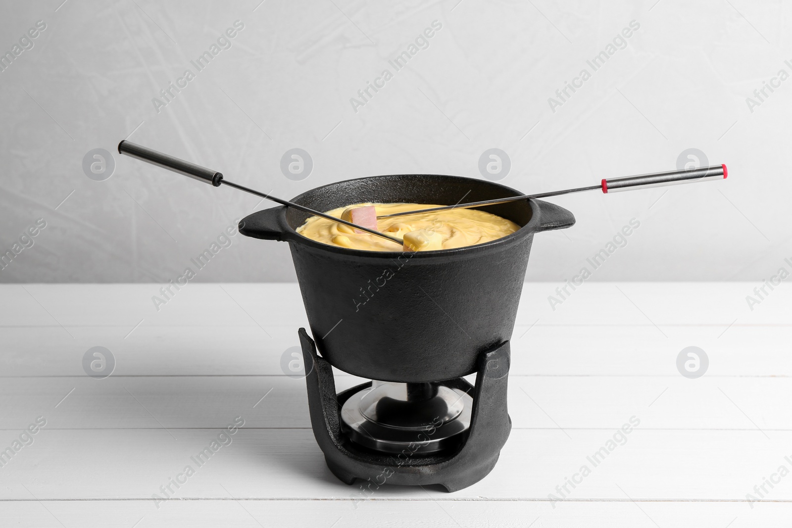 Photo of Fondue pot with tasty melted cheese, forks and ham on white wooden table