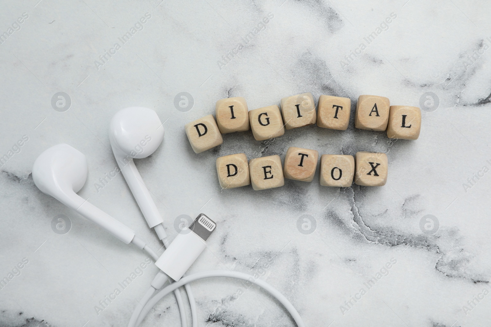 Photo of Cubes with phrase DIGITAL DETOX and earphones on white marble table, flat lay