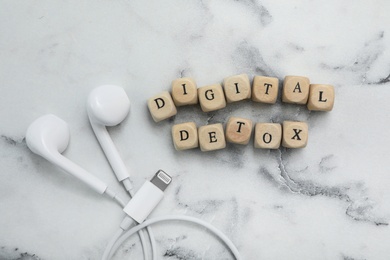 Photo of Cubes with phrase DIGITAL DETOX and earphones on white marble table, flat lay