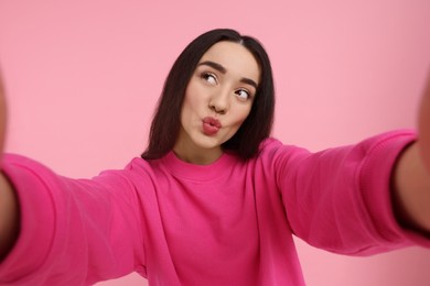 Photo of Young woman taking selfie and blowing kiss on pink background