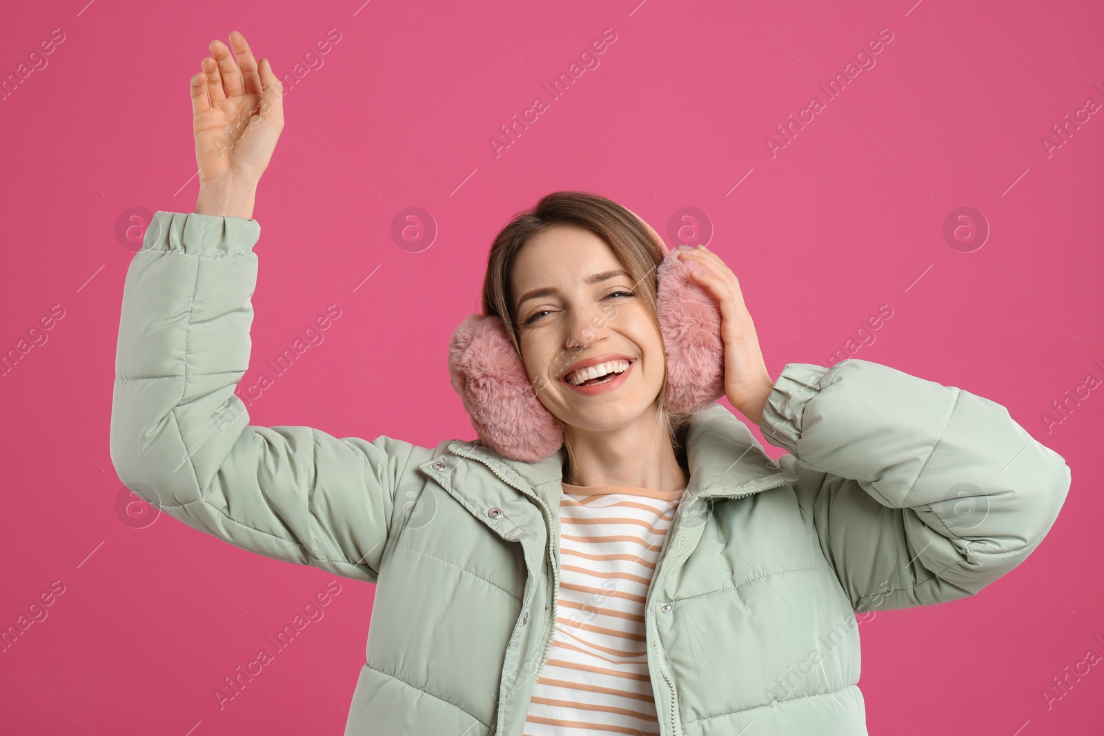 Photo of Happy woman wearing warm earmuffs on pink background