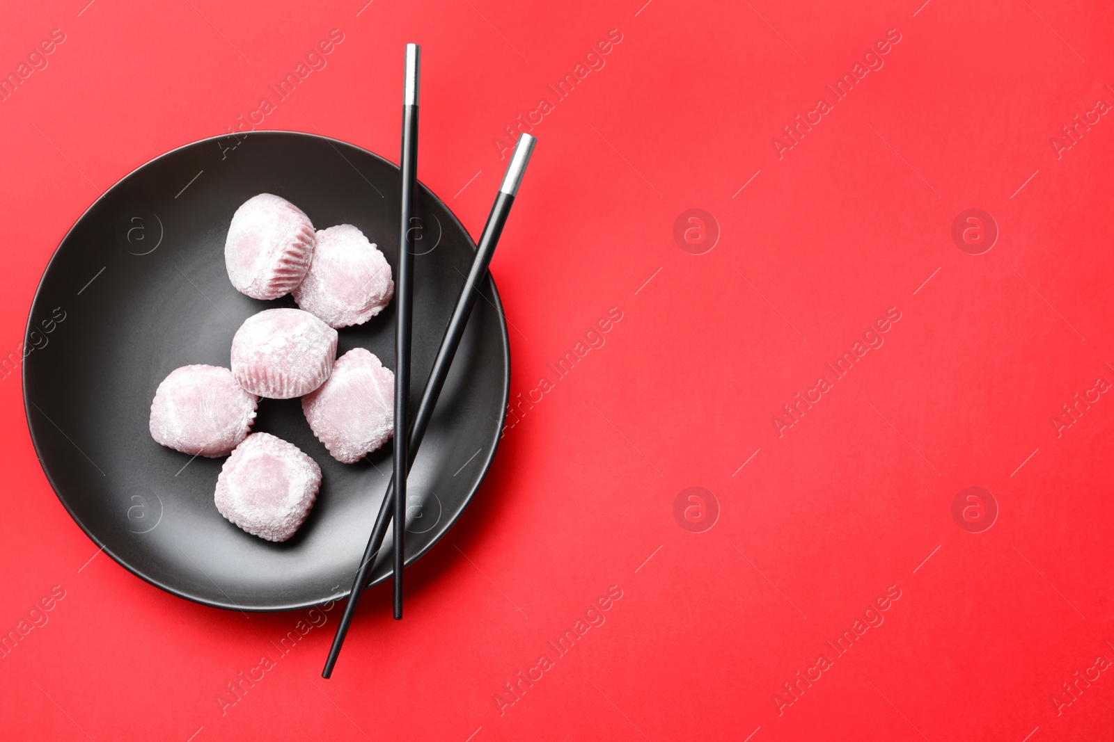 Photo of Black plate with delicious mochi and chopsticks on red background., top view. Space for text