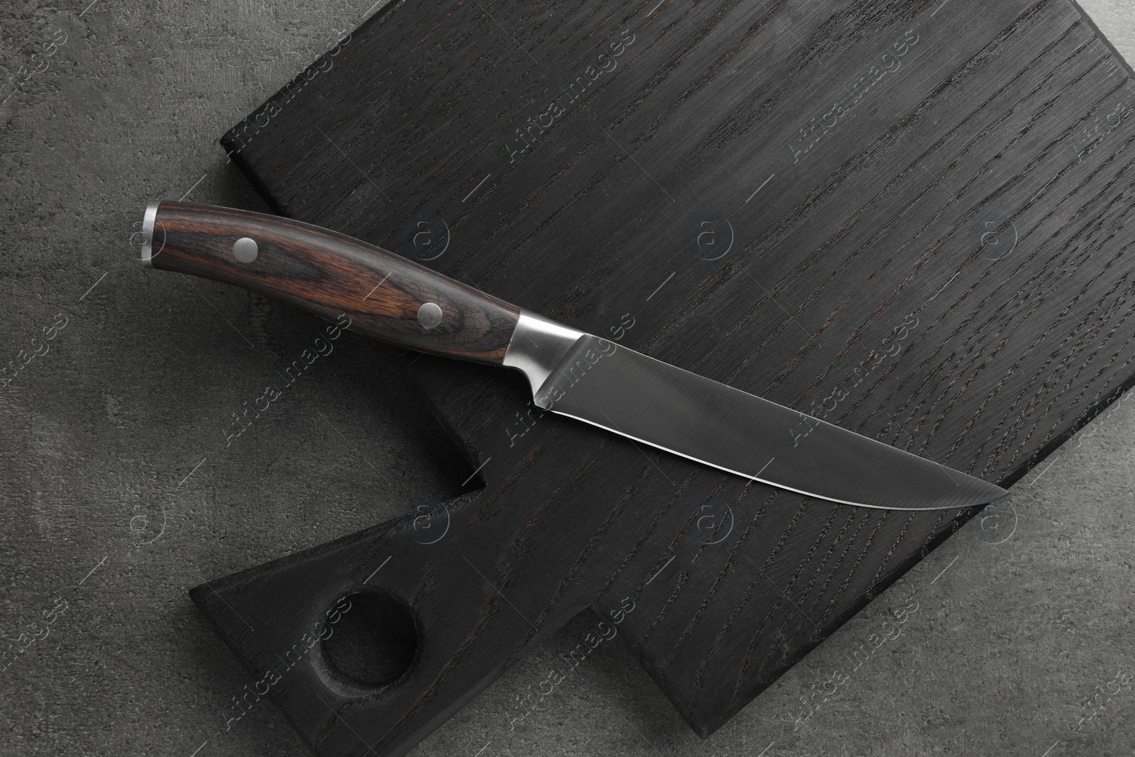 Photo of Knife and black wooden board on grey textured table, top view