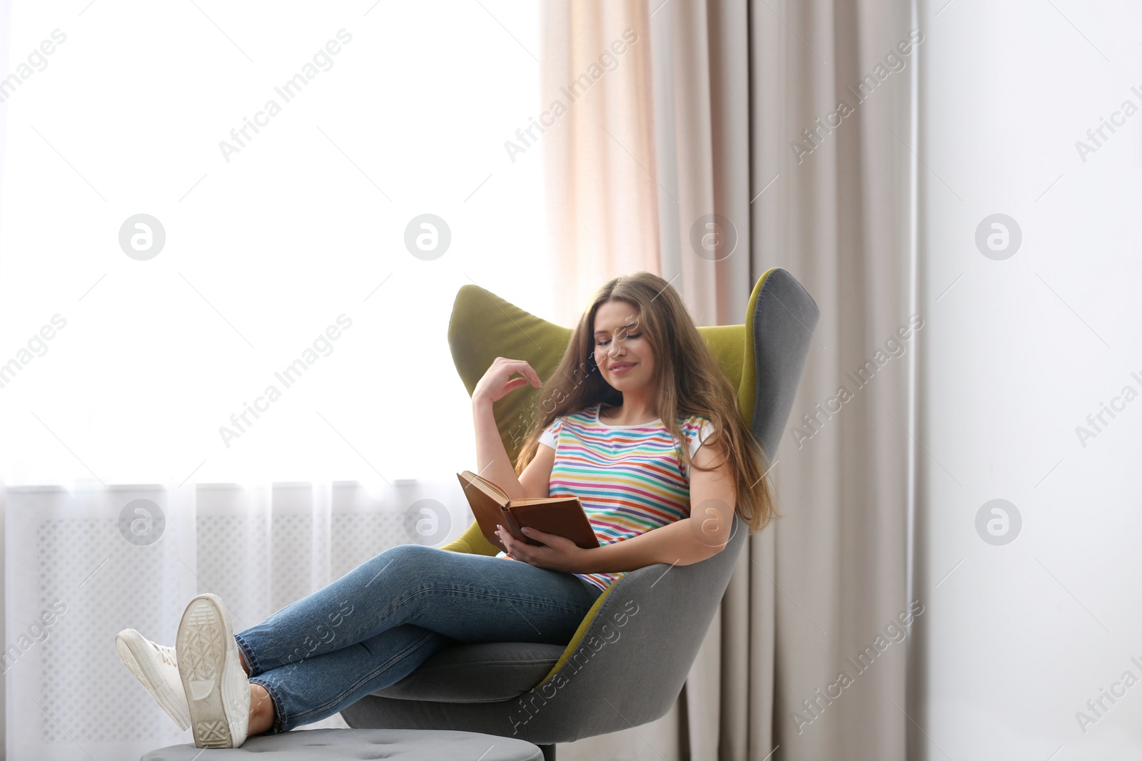 Photo of Young woman reading book in armchair at home