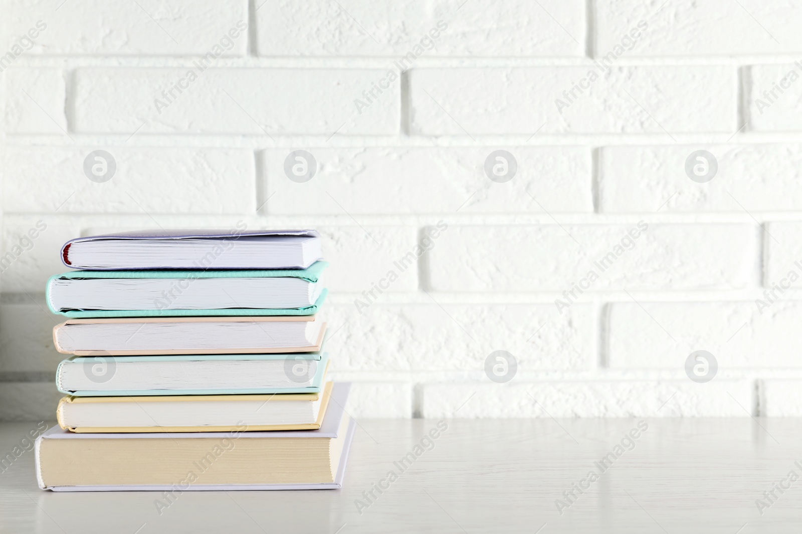 Photo of Stack of hardcover books on table against brick wall, space for text