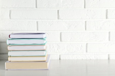 Photo of Stack of hardcover books on table against brick wall, space for text