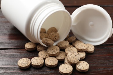 Photo of Bottle and vitamin pills on wooden table, closeup