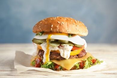 Photo of Tasty burger with fried egg on parchment against color background