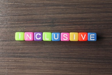 Photo of Colorful cubes with word Inclusive on wooden table, flat lay