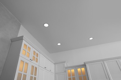 Photo of Ceiling with modern spot lamps and furniture in stylish kitchen, low angle view