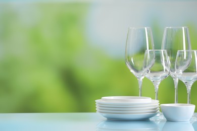 Set of many clean dishware and glasses on light blue table against blurred green background. Space for text