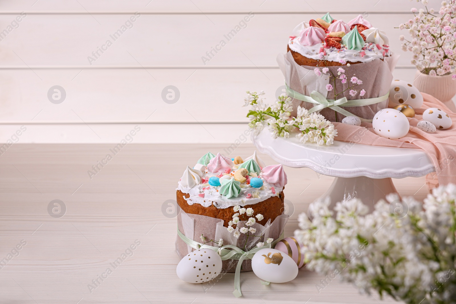 Photo of Traditional Easter cakes with meringues and painted eggs on white wooden table, space for text