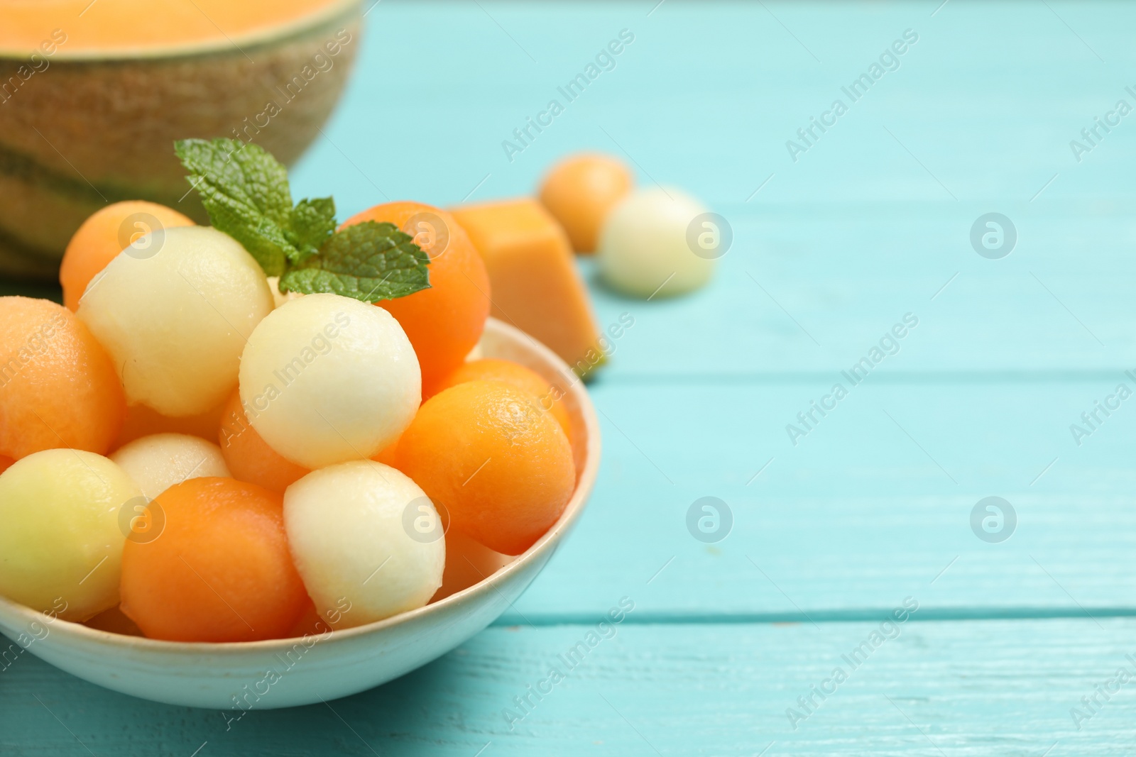 Photo of Melon balls and mint in bowl on light blue table, closeup. Space for text