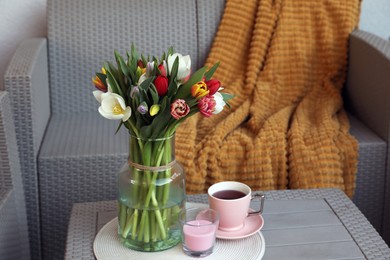 Beautiful bouquet of colorful tulips, cup with drink and candle on rattan garden table