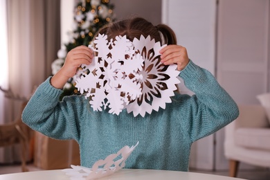 Photo of Cute little girl with paper snowflakes at table indoors