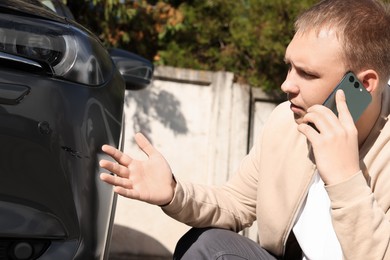Photo of Man talking on phone near car with scratch outdoors
