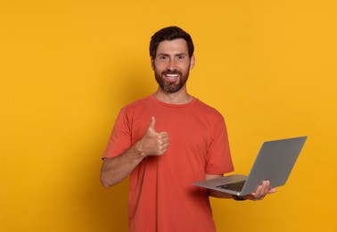Handsome man with laptop showing thumb up gesture on orange background