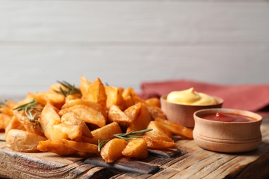 Photo of Baked potatoes served with rosemary, ketchup and mayonnaise on wooden board. Space for text