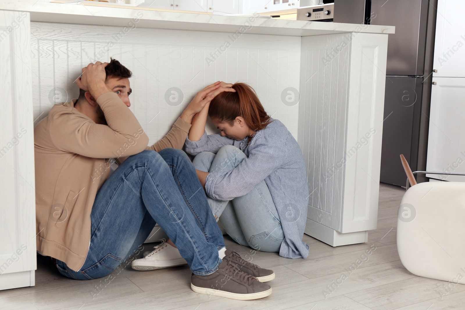 Photo of Scared couple hiding under table in kitchen during earthquake