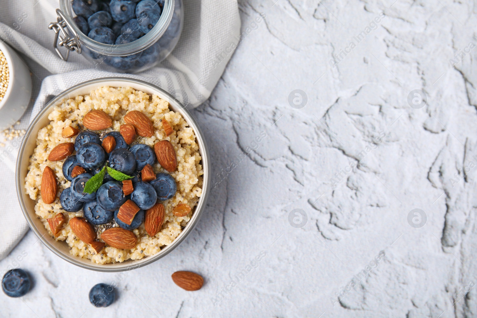 Photo of Bowl of delicious cooked quinoa with almonds and blueberries on white textured table, flat lay. Space for text