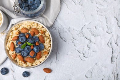 Bowl of delicious cooked quinoa with almonds and blueberries on white textured table, flat lay. Space for text