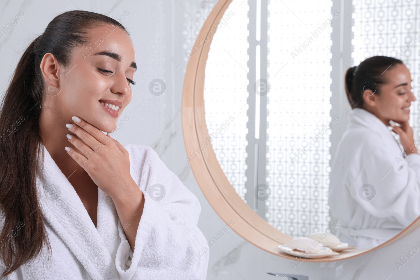 Photo of Beautiful young woman with perfect skin near mirror in bathroom. Facial wash