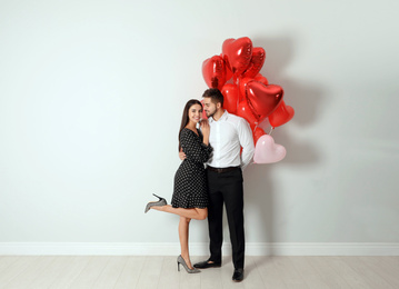 Photo of Happy young couple with heart shaped balloons near light wall. Valentine's day celebration