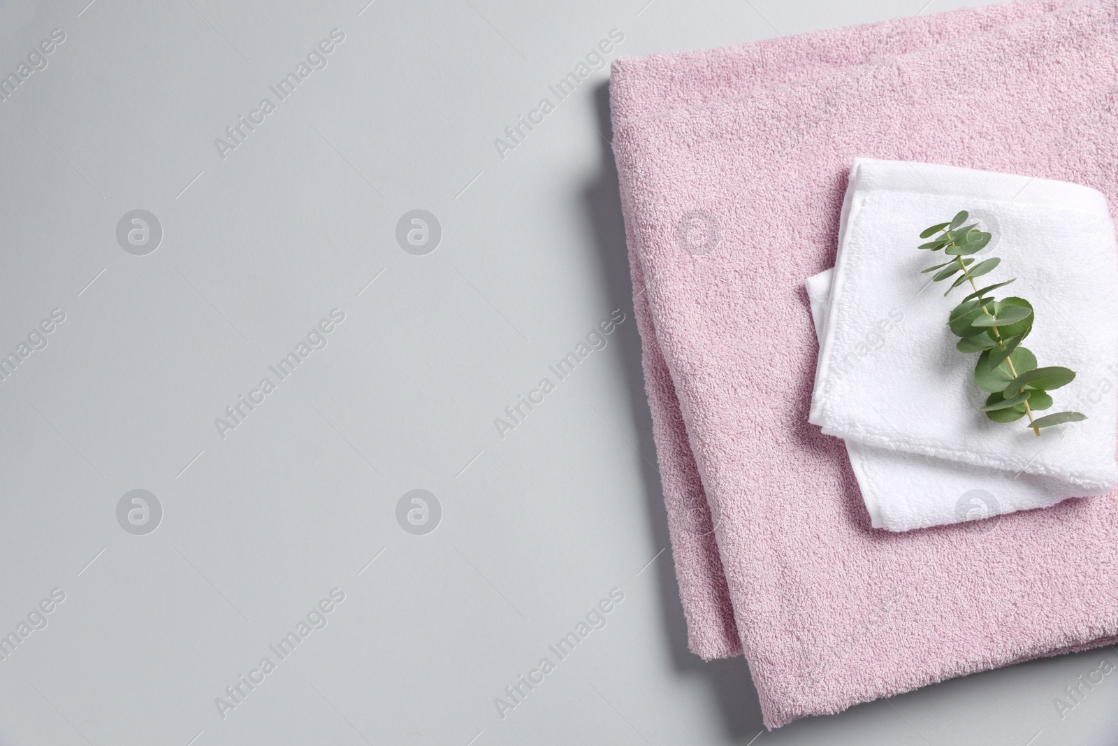 Photo of Soft folded towels with eucalyptus branch on light grey background, top view. Space for text