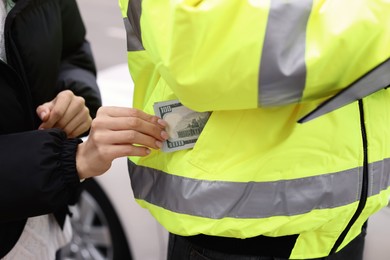 Photo of Woman putting bribe into police officer's pocket, closeup