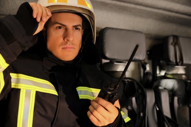 Firefighter in uniform with portable radio set on backseat of fire truck