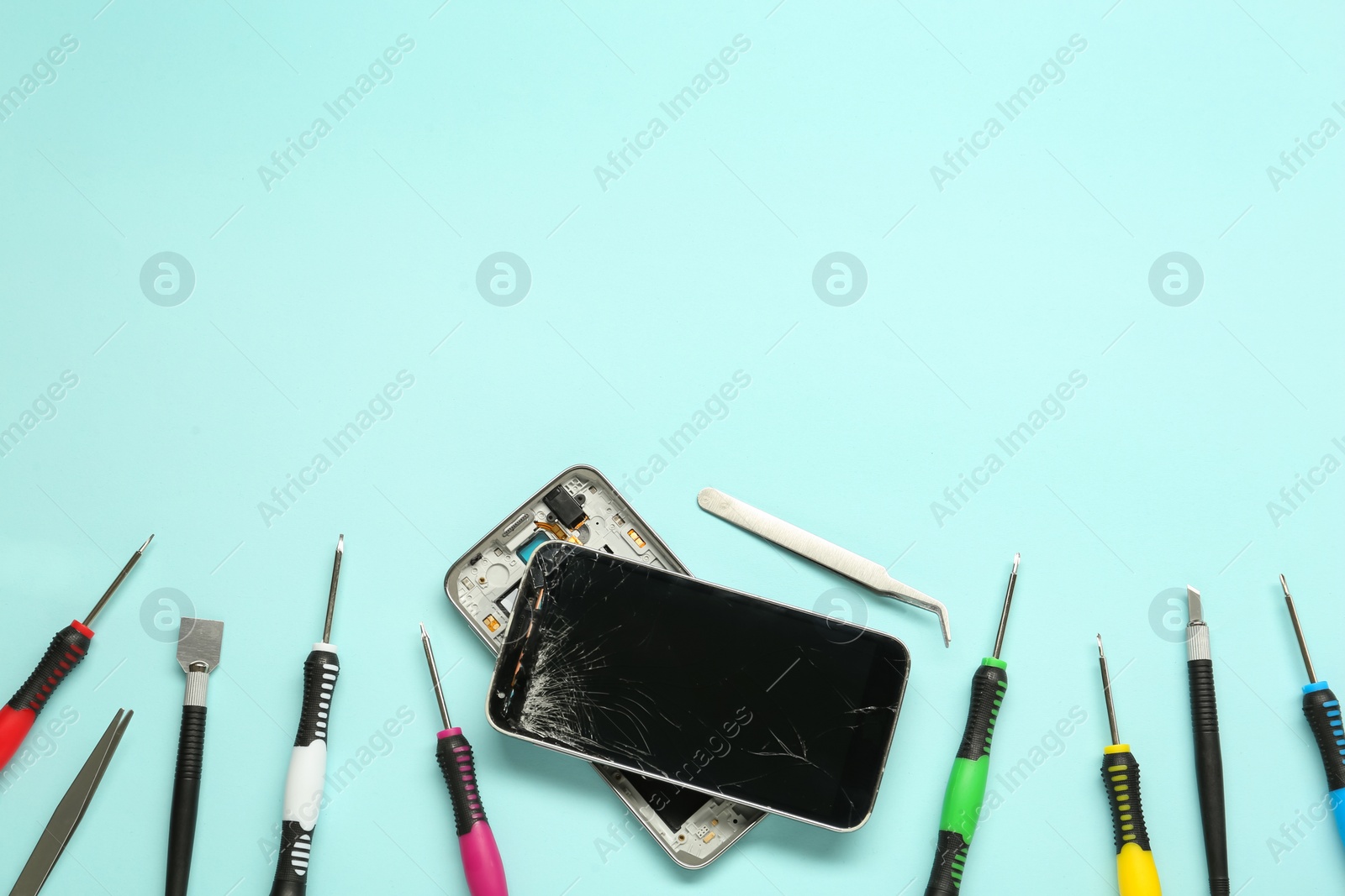 Photo of Damaged smartphone and repair tool set on light blue background, flat lay. Space for text