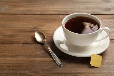 Photo of Tea bag in cup of hot water on wooden table. Space for text